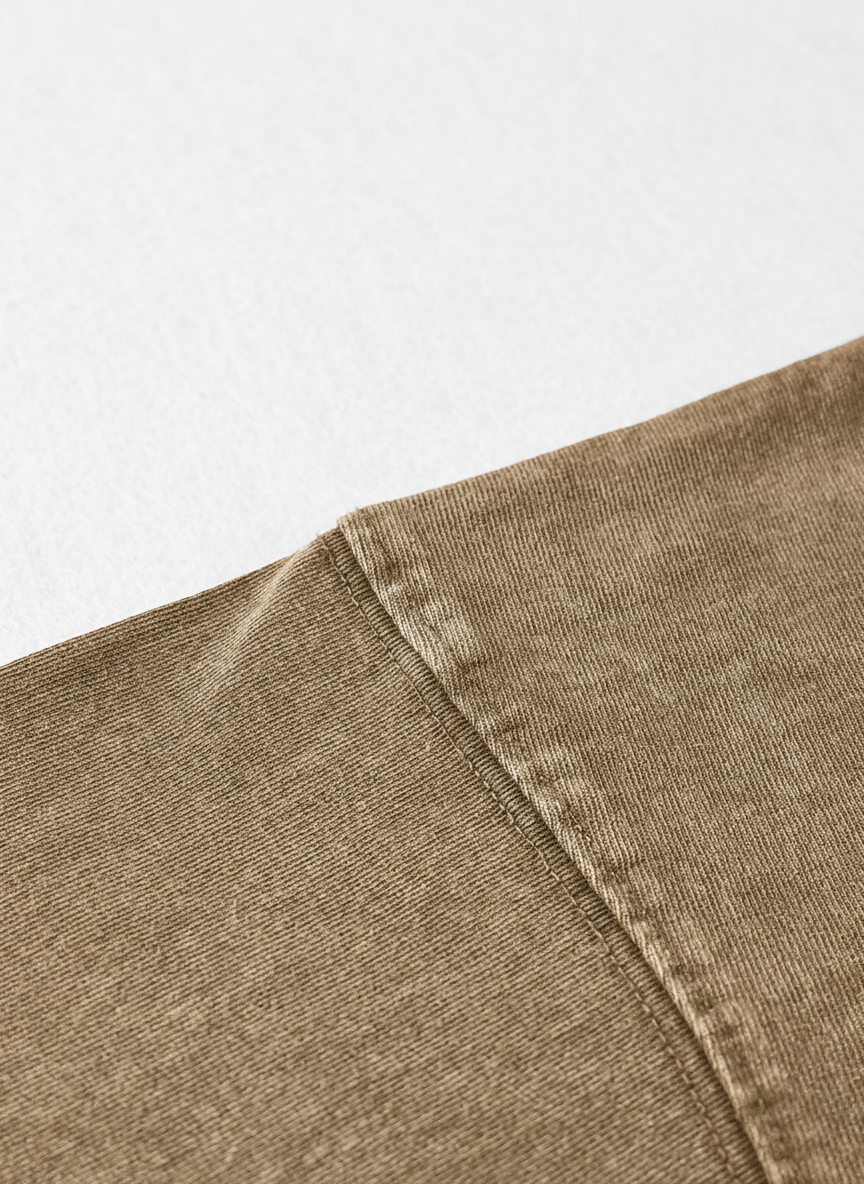 A close-up view of a piece of brown fabric, possibly denim, with a slight crease visible.