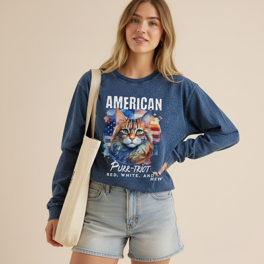 Woman wearing a blue sweatshirt with a cat graphic and text, holding a beige tote bag.