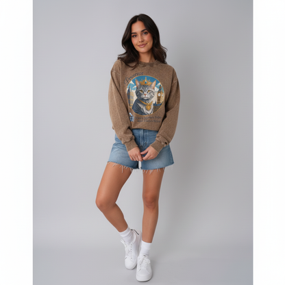 Woman wearing a brown sweater with a cat graphic, denim shorts, and white sneakers on a gray background
