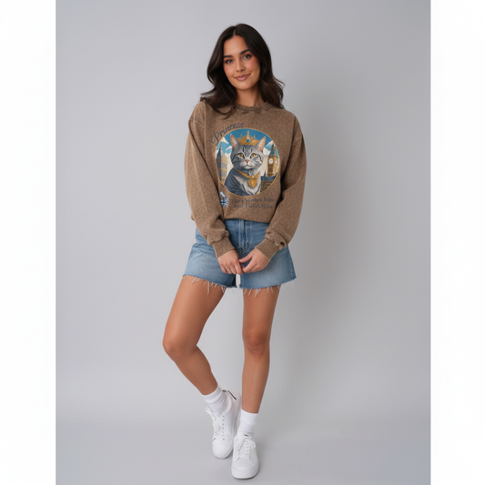 Woman wearing a brown sweater with a cat graphic, denim shorts, and white sneakers on a gray background