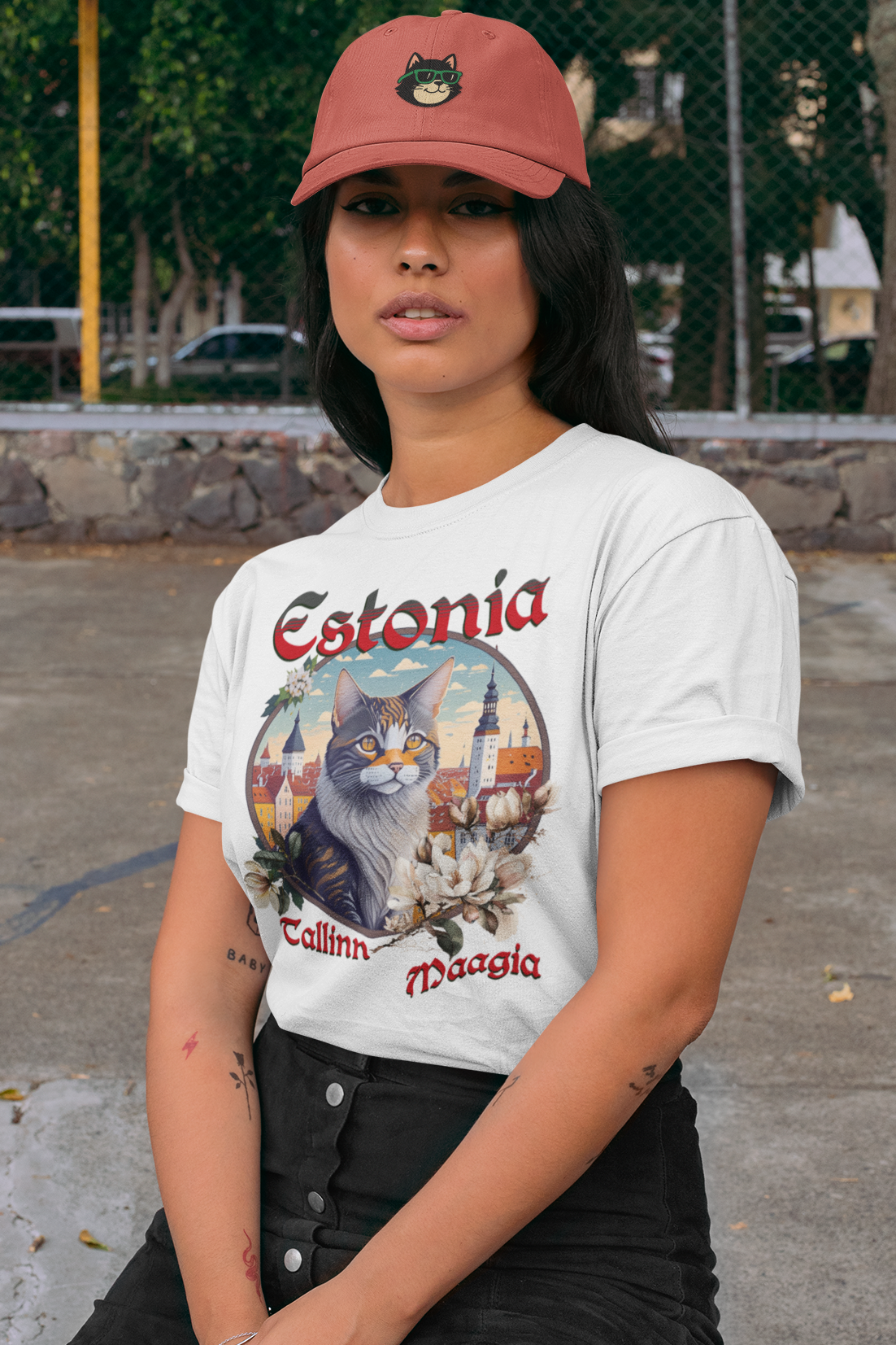 Woman wearing a white t-shirt with 'Estonia' design and a red cap, sitting outdoors.